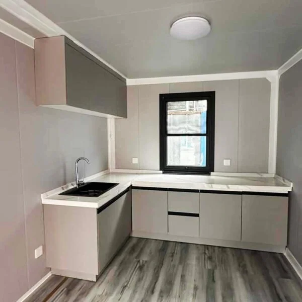 Factory-fitted kitchen in expandable container home — grey units, marble-effect worktop, black-frame window