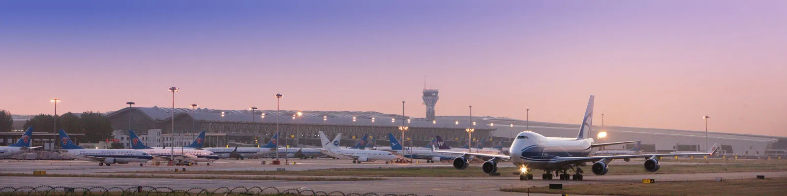Panoramic dusk view of the apron at Zhengzhou Xinzheng International Airport (CGO), cargo and passenger aircraft lined up before the terminal and control tower